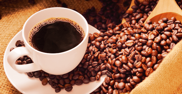 a white cup of coffee sitting next to a spilled bag of roasted coffee beans